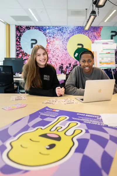 Twee studenten zitten achter een tafel met één laptop.