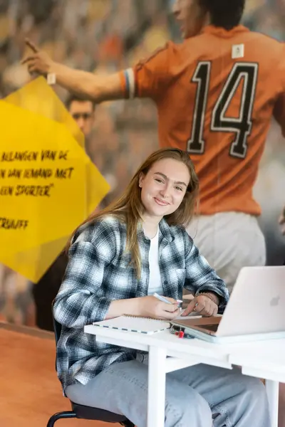 Student zit lachend achter een laptop aan een bureau.