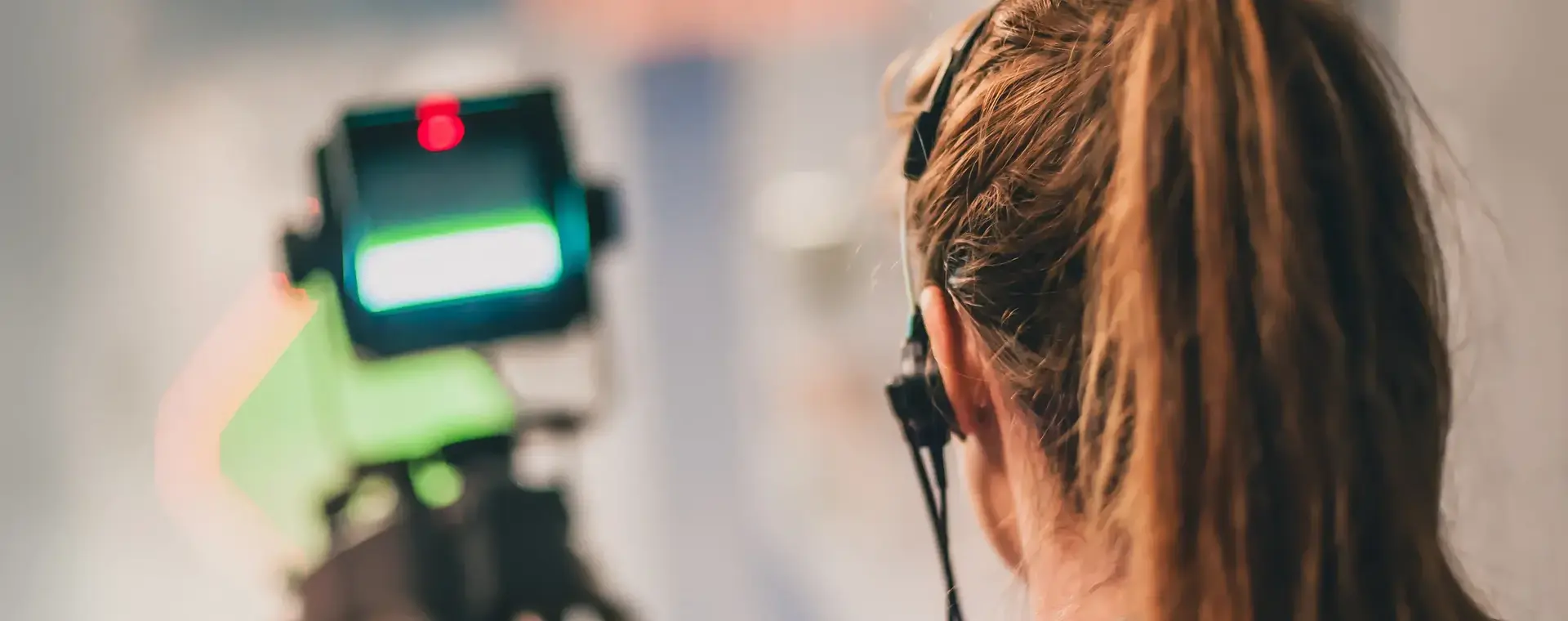 Meisje met staart en koptelefoon staat in een tv studio. Op de achtergrond zie je een tv camera. 
