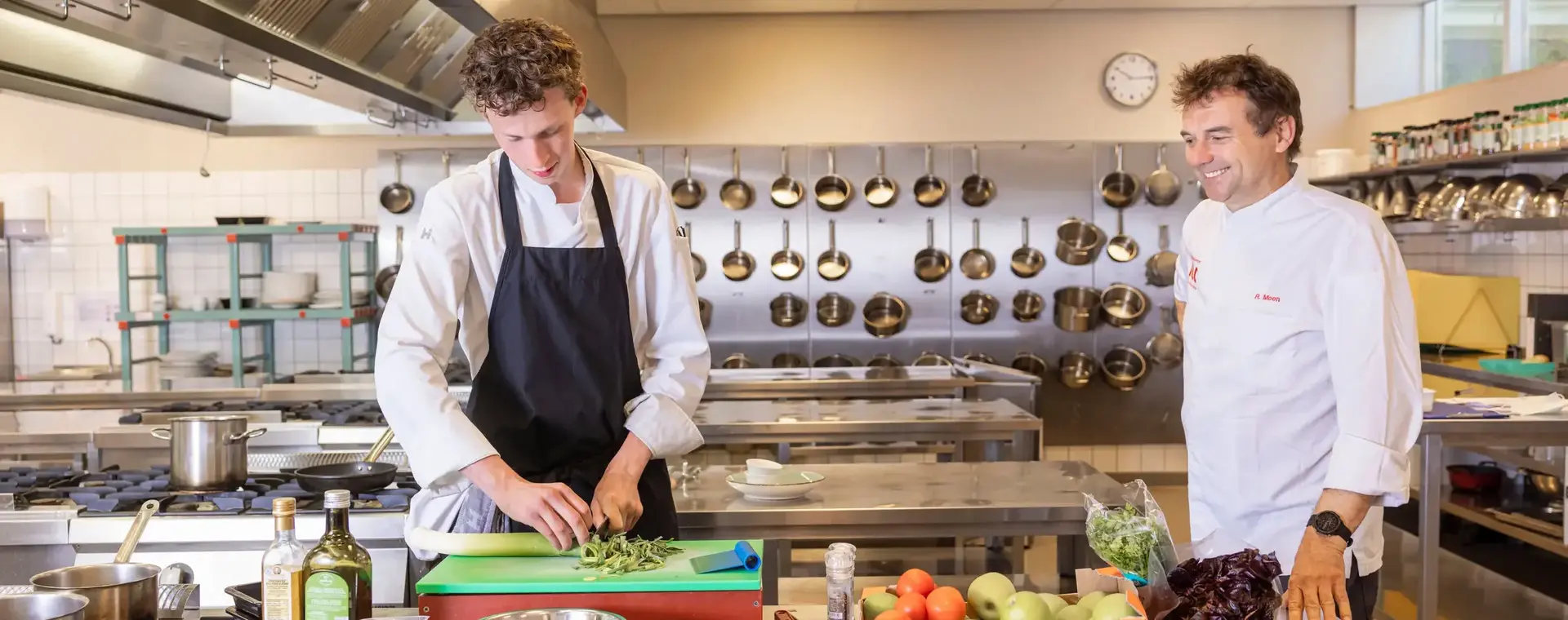 Student en docent bereiden samen een maaltijd in professionele keuken.