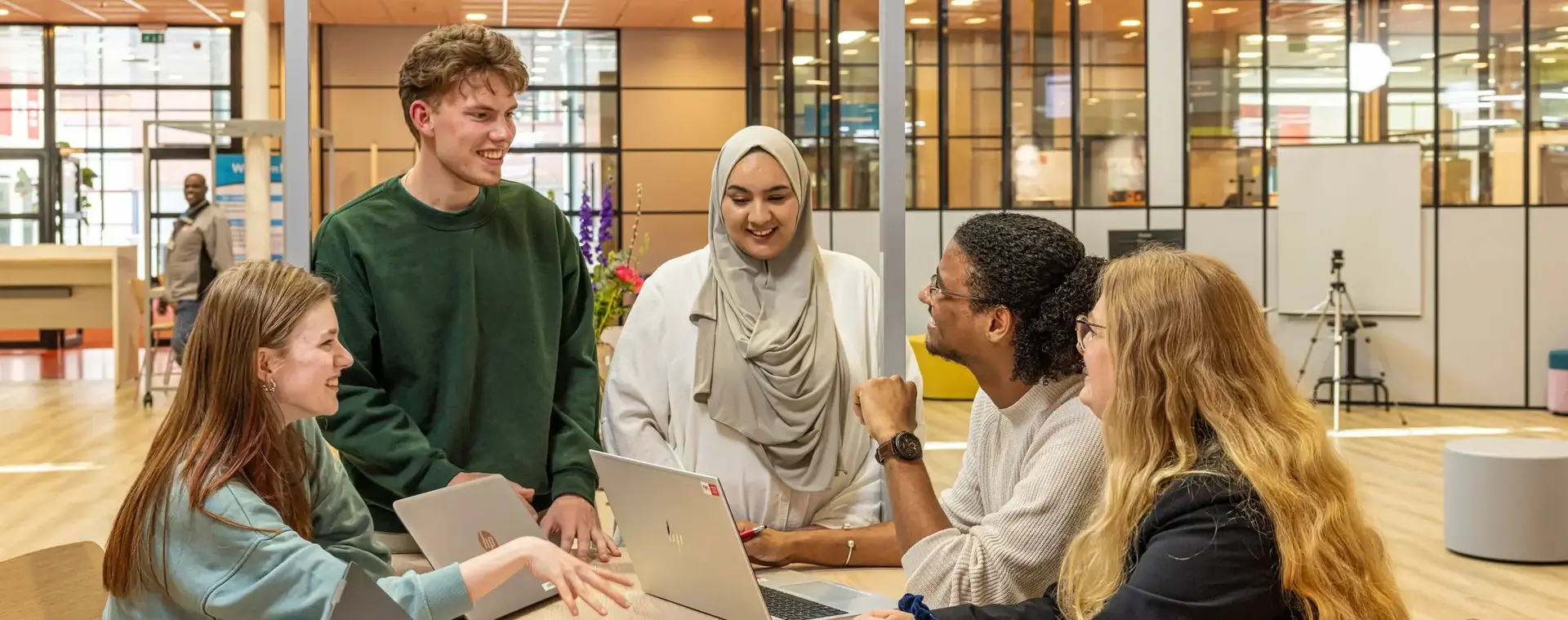 Groep studenten werkt samen aan een opdracht met laptops en mappen.