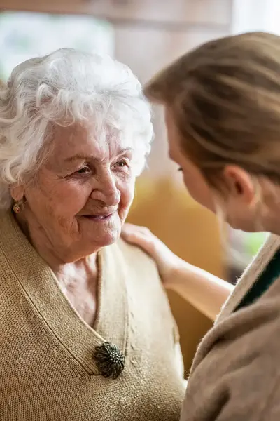 Vrouw houdt haar hand op de schouder van bejaarde vrouw