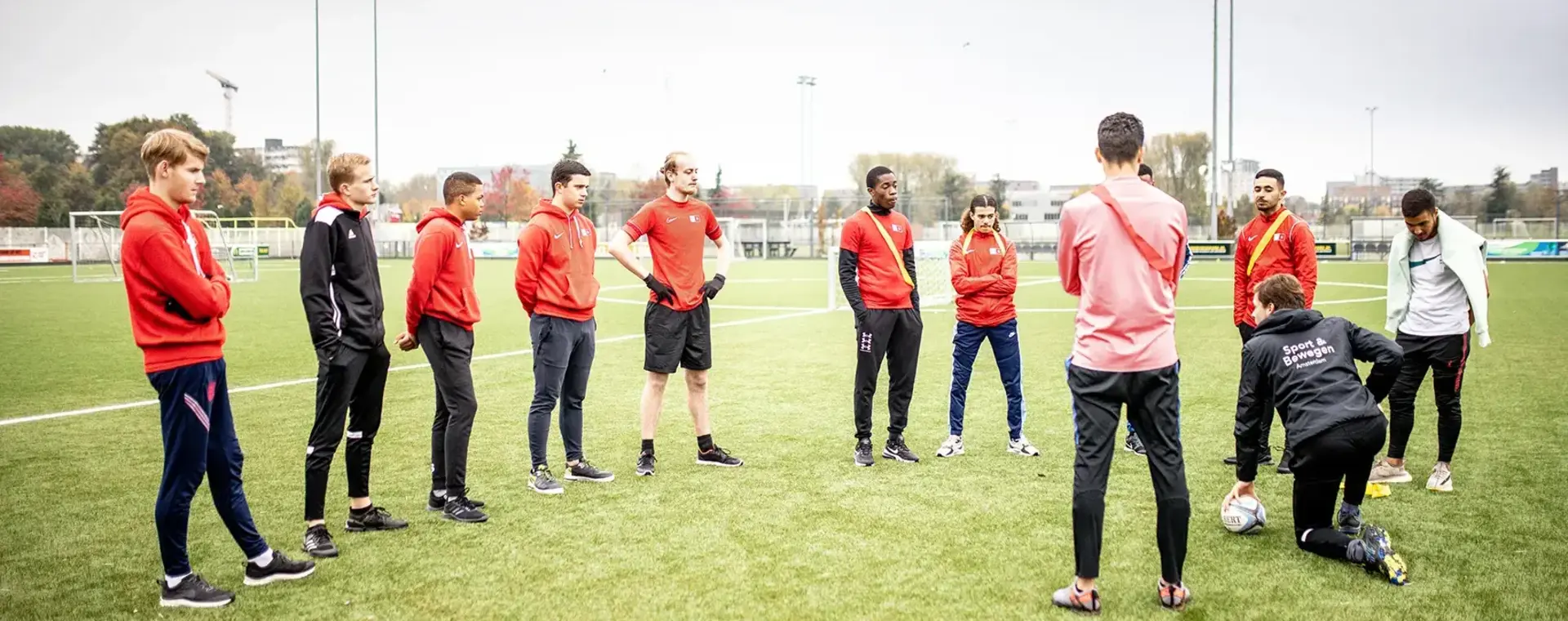 Voetballers staan in een halve cirkel en luisteren naar hun coach.