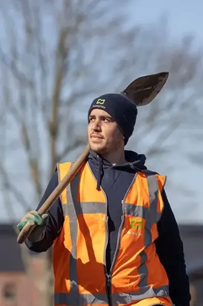 Man met muts en oranje veiligheidsvest en schep op zijn schouder